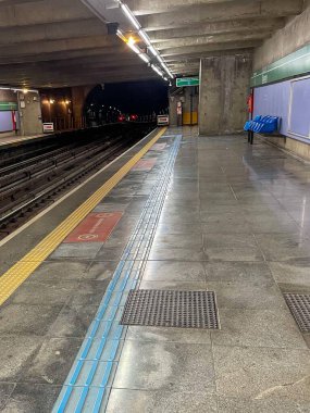 Yerden yansıyan parlak kiremitleri, tabelası ve ışıklandırması olan terk edilmiş bir metro istasyonu. Soldaki izler, sağdaki boş koltuklar kentsel bir his ve hafif ışıklandırma..