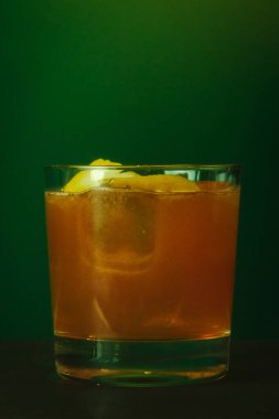 Kehribar renginde ferahlatıcı bir kokteyl. Buzlu ve limonlu bir bardakta servis ediliyor. Yeşil arka planda.. 