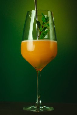 A vibrant orange cocktail served in a tall glass, garnished with fresh mint leaves, set against a green background.  clipart