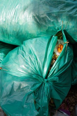 Bahçe atıklarıyla sıkıca paketlenmiş, ağaçlar ve bitki örtüsüyle çevrili bir yığın yeşil plastik poşet.. 