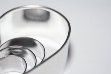 Beyaz arka planda gümüş metal kalp şeklindeki kurabiye kesicinin makro görüntüsü..