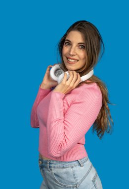 Kablosuz kulaklık takan mutlu genç kadın mavi arka planda müziğin keyfini çıkarıyor.