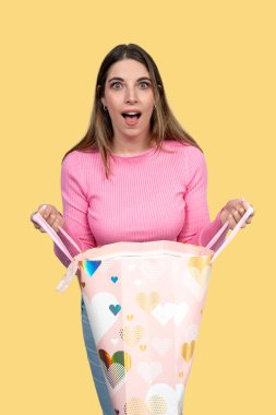 Sevgililer Günü hediyesi paketi açan, kalp şekilli ve hayret verici bir genç kadının stüdyo fotoğrafı.