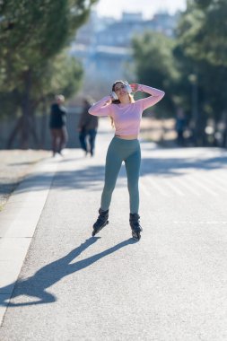 Şehir parkında paten kayan ve kulaklıkla müzik dinleyen genç bir kadın.