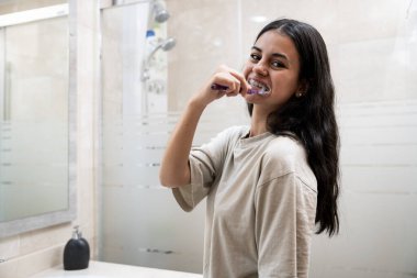 Dişlerini fırçalayan genç esmer kadın.