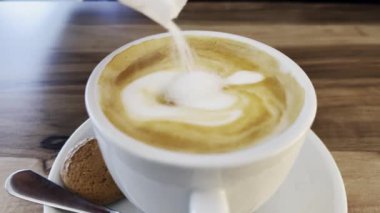 Beyaz seramik kap kapuçino ile latte sanat, küçük bir bisküvi ve şeker dökülüyor