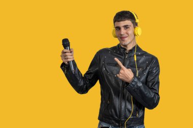 Siyah deri ceket giyen beyaz bir adam ve sarı arka planda parmağı olan bir mikrofon tutan sarı kulaklık.