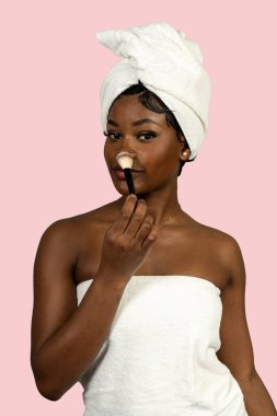 Havluya sarılmış, fırçayla makyaj yapan bir kadın.