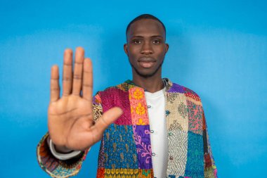 Kendine güveni tam genç bir adam el hareketini durduruyor, canlı mavi arka planda reddediyor ya da onaylamıyor.