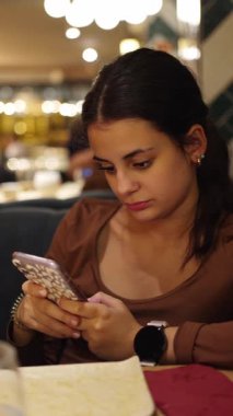 Restoranda cep telefonu kullanan, yemeğin tadını çıkaran ve bağlantıyı koparmayan bir genç.