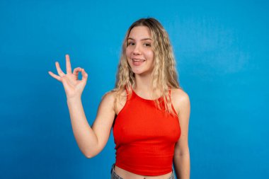 Gülümseyen kadın mavi arka planda iyi bir işaret veriyor.