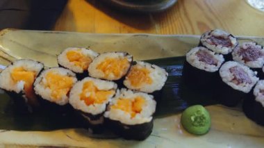 Yemek çubuğu kullanan bir kadın, Japon restoranında wasabi ve soya sosuyla servis edilen çeşitli suşi rulolarını yemeye hazırlanıyor.