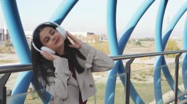 Kablosuz kulaklık takan genç bir kadın modern şehir ortamında müzik dinlemekten hoşlanıyor