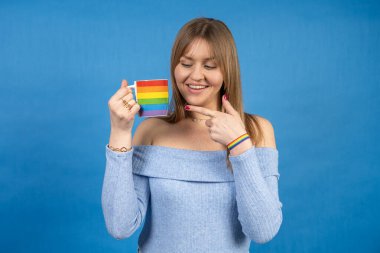 Gökkuşağı kupası ve bileziğini gösteren genç bir kadının lgbtq + gururunu kutlarken çekilmiş bir fotoğrafı.