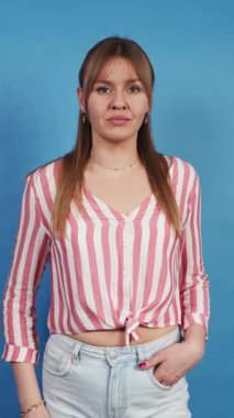 Mavi stüdyo arka planında dur işareti yapan ciddi bir genç kadın.