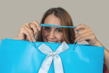 Beyaz ve altın kurdeleli açık mavi alışveriş çantasının arkasına saklanan gülümseyen kadın.