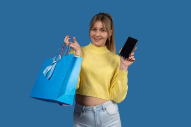 Akıllı telefon ekranı gösteren ve başarılı online alışverişin ardından alışveriş torbası tutan mutlu müşteri