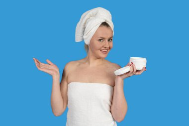 Havluya sarılmış bir kadın, duş aldıktan sonra bir kavanoz nemlendirici krem tutuyor. Vücut bakımını ve sağlığını destekliyor.