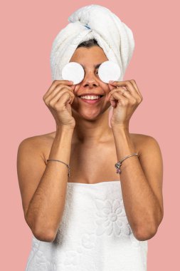 Banyo havlusu takan mutlu bir kadın. Gözlerinin üzerinde iki pamuk tutuyordu. Duştan sonra cilt bakımının keyfini çıkarıyordu.