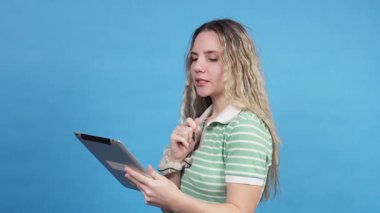 Elinde dijital tablet ve kalem tutan genç bir kadın mavi arka planda yeni fikirler üretiyor.