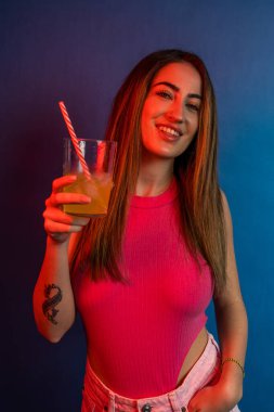 Şık genç bir kadın hayat dolu bir gece sahnesinde ferahlatıcı bir içecekten hoşlanıyor.