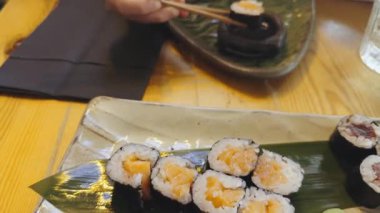 Japon restoranındaki tabaktan suşi rulosu toplamak için çubuk kullanan biri.