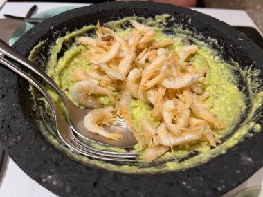 Kızarmış karidesli kremalı guacamole, geleneksel bir taş kasede servis ediliyor, tadını çıkarmaya hazır.