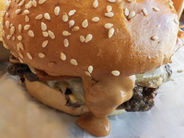 Susamlı çörek ve erimiş peynirle soslu sulu bir hamburgerin yakın çekimi.