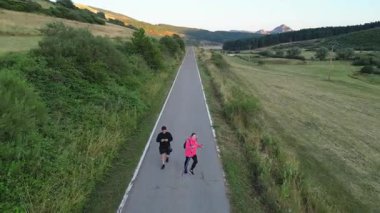İki sporcu kırsalda asfalt bir yolda yürüyor.