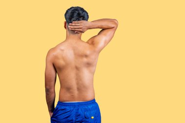 Tişörtsüz bir adamın elleriyle kafasına dokunuşunun arka görüntüsü.