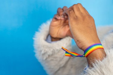 Bileğinde gökkuşağı bileziğini gösteren kişi mavi arkaplanda lgbtq + gururu simgeliyor