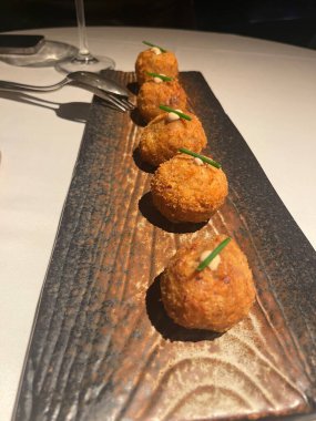 Frenk soğanı ve aioli ile süslenmiş beş altın sarısı arancini, güzel bir yemek ortamında kırsal bir tabakta servis edilir.