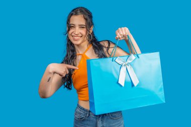 Gülümseyen genç bir kadın beyaz kurdeleli bir alışveriş torbasını işaret ediyor, alışverişler, hediyeler, alışveriş konsepti
