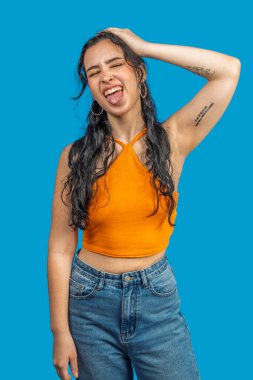 Dövmeleri olan kaygısız genç bir kadın. Dilini gösteriyor ve uzun siyah saçlarını tutuyor. Oyuncu ve asi tavırlar sergiliyor.