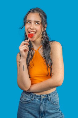 Neşeli genç bir kadın kalp şeklinde bir lolipopun tadını çıkarıyor, neşeli ve kaygısız bir tavır sergiliyor.