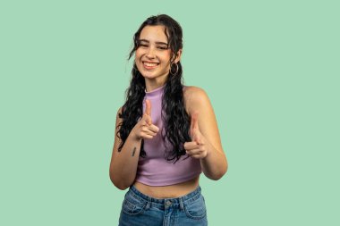 Neşeli genç bir kadın parmaklarını göstererek silahların simülasyonunu yapıyor ve yeşil arka planda gülümsüyor