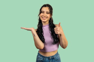 Genç bir kadın baş parmaklarıyla bir şey gösterip öneriyor.