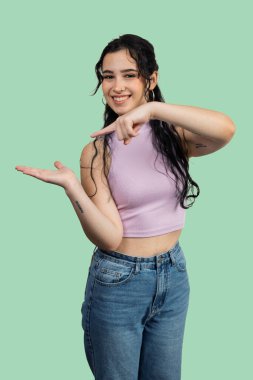 Gülümseyen genç bir kadın, yeşil bir arka planda, avuçlarını açık bir şekilde gösteriyor ve gösteriyor.