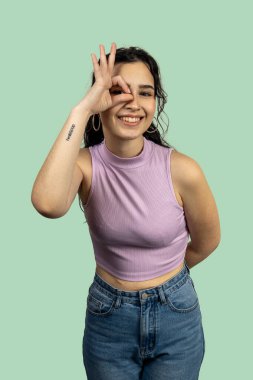 Stüdyo portresi, yeşil bir arka planda eli ile iyi bir jest yapan neşeli bir genç kadın.