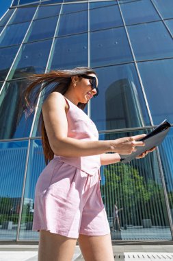 Şehirde yürüyen ve modern bir ofis binasının önünde doküman okuyan iş kadını.