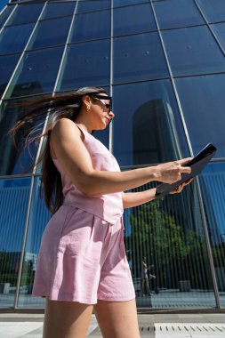 Modern bir ofis binası önünde yürüyen ve belgeleri okuyan iş kadını, çağdaş profesyonel