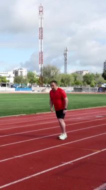 Kırmızı bir atletizm pistinde koşan orta yaşlı bir adam.