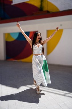 Uzun kahverengi saçlı tasasız genç bir kadın dans yoluyla neşe ve özgürlük ifade ediyor, şık çizgili bir kıyafet giyiyor.