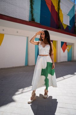 Şık bir model gözlerini güneşten koruyor ve renkli renkli bir şehir zeminine karşı şık bir kıyafet sergiliyor.