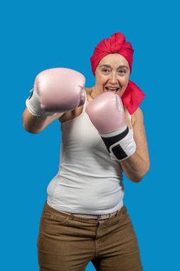 Pembe boks eldiveni giyen güçlü kadın dövüşüyor ve mavi arka plana karşı iradesini gösteriyor.