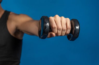 Sporcunun mavi arkaplan üzerinde çalışırken dambılı kaldırışını kapat