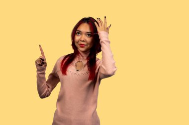 Düşünceli bir kadın, sarı arka planda parmaklarıyla hareket ediyor.