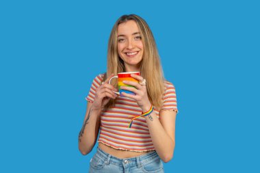 Gurur ayını kutlayan genç bir kadın, gökkuşağı bardağında kahvenin tadını çıkaran ve gökkuşağı bileziği takan, lgbtq + desteği ve eşitliği simgeleyen genç bir kadın.