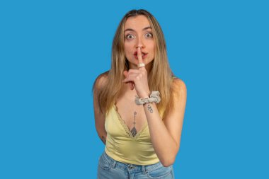 Stüdyo portresi. Dövmeleri olan genç bir kadın. Parmağı dudaklarında sessiz bir jest yapıyor.