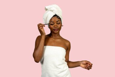 Duştan sonra makyaj yapan, kafasına havlu ve havlu takan genç siyahi bir kadının güzellik rutini.